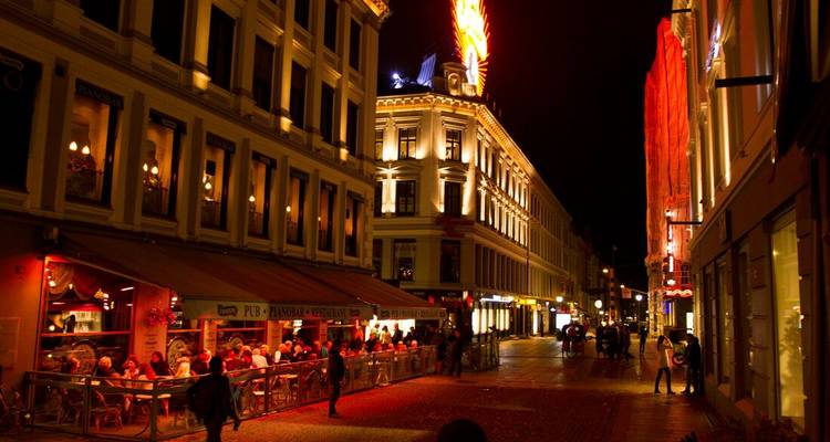Rue animée éclairée la nuit avec des gens qui dînent dehors.