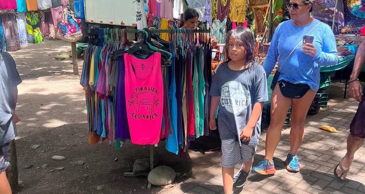 Marché en plein air avec des gens et des étals de vêtements colorés.