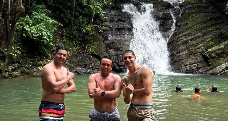 Trois hommes posant devant une cascade avec une végétation luxuriante autour.