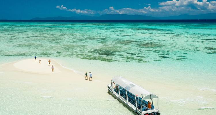 Barco cerca de una pequeña isla de arena rodeada por agua turquesa.
