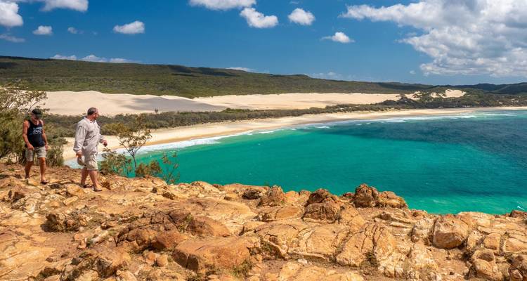 Dos personas caminando por el borde de un acantilado con vista al mar.