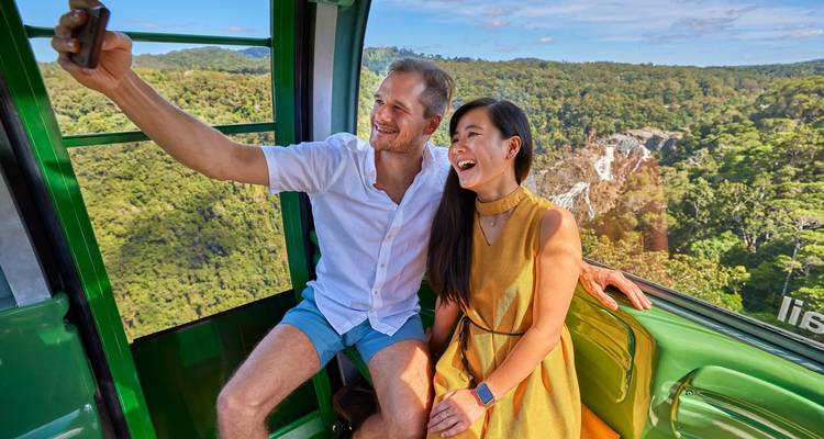 Pareja tomándose una selfie en una góndola sobre vegetación exuberante y una cascada.