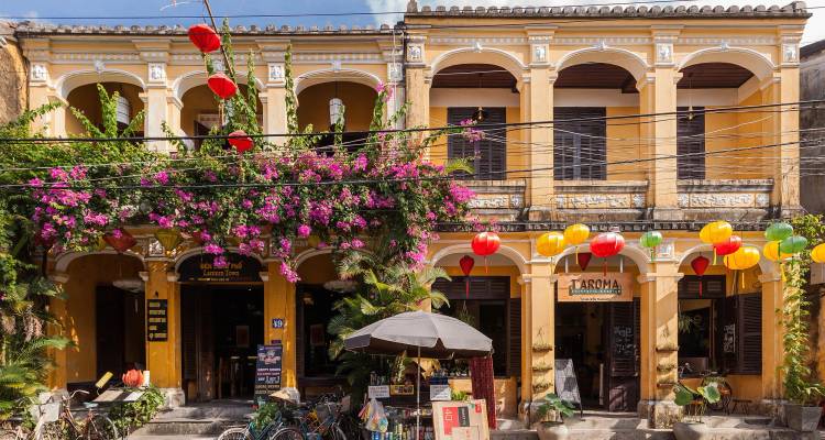 Traditional yellow buildings with lanterns and vines in a historic area.