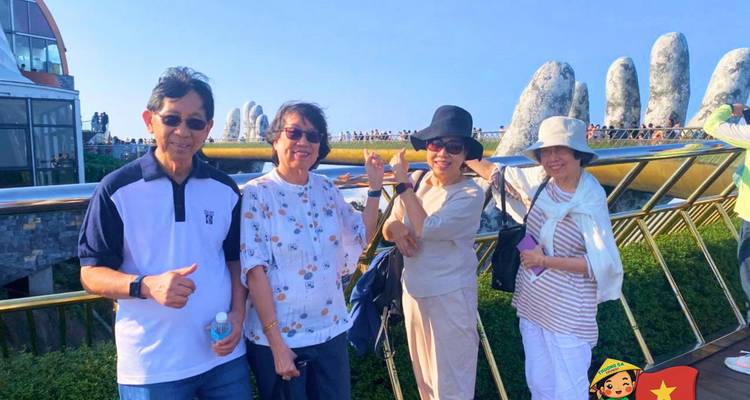 Cuatro mujeres sonriendo en el Puente Dorado de Vietnam con las gigantescas manos de piedra visibles detrás de ellas.