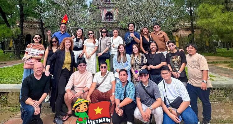 Gran grupo de turistas reunido frente a una antigua torre pagoda ubicada entre vegetación.