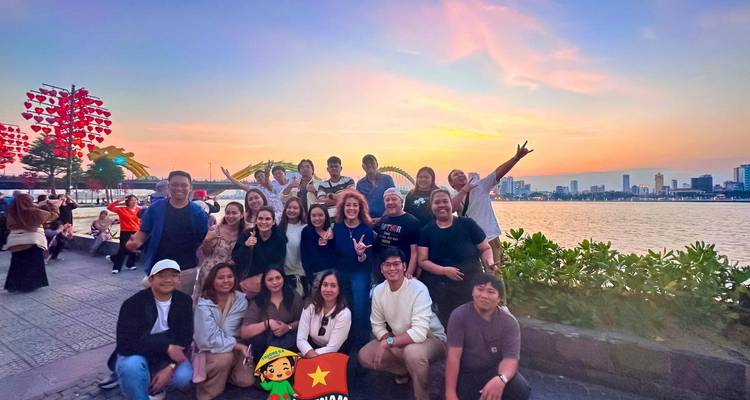 Foto grupal al atardecer en la ribera con el Puente del Dragón de Da Nang brillando en la distancia.