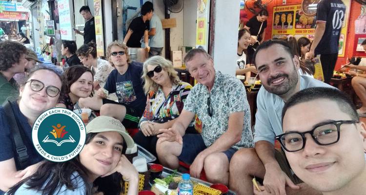 Group selfie of people sitting at a street market stall.