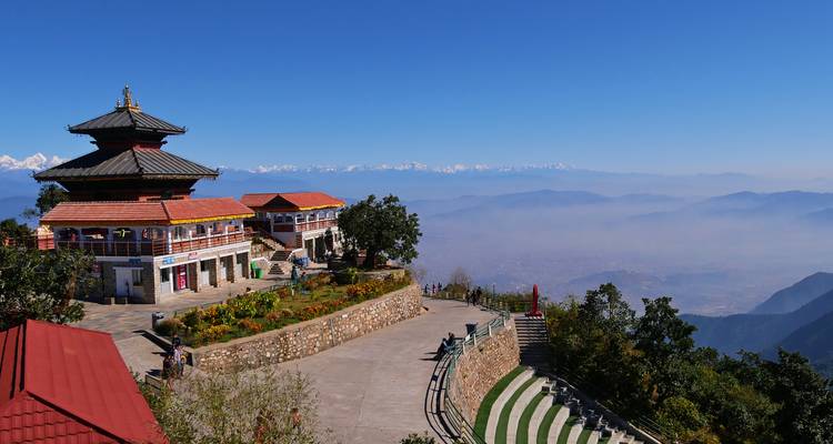 Vue panoramique depuis une colline surplombant une vallée avec l'Himalaya en arrière-plan.