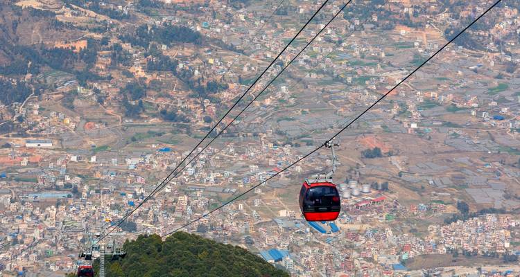 Téléphériques au-dessus d'une vallée avec un paysage urbain en contrebas.