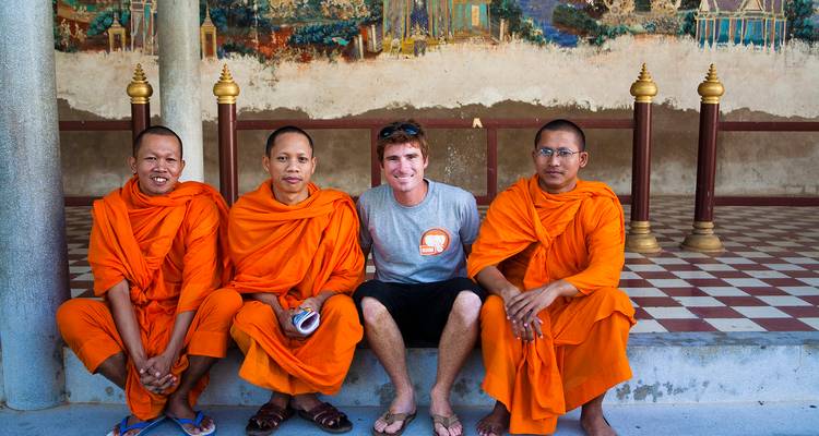 Group of Buddhist monks and a tourist posing together by a decorated wall.