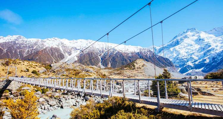 Pont suspendu avec des montagnes enneigées en arrière-plan.