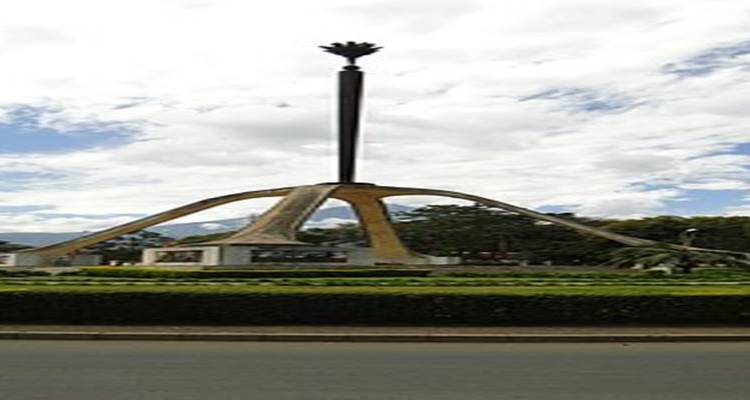 Monumento de una estructura central con una aguja alta, vegetación y un cielo azul.