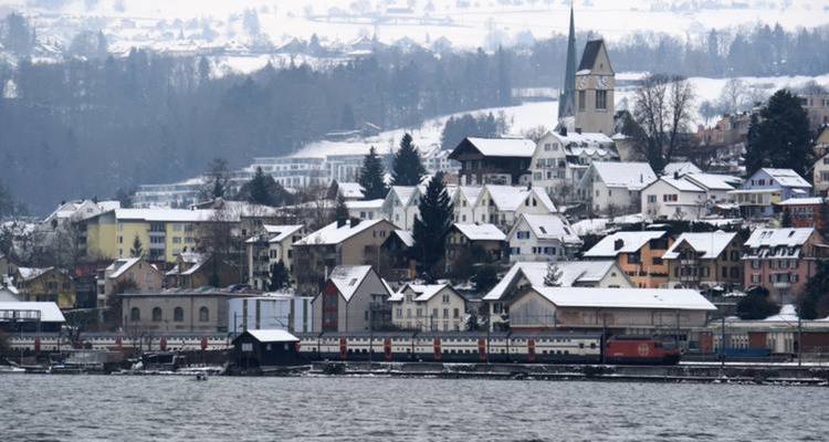 Ville enneigée avec une église au bord d'un lac.