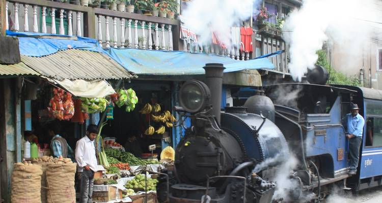 Un train à vapeur traversant une zone de marché avec des vendeurs.