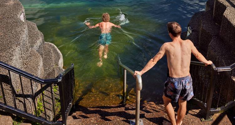 Deux personnes au bord d'un lac rocheux, l'une nageant.