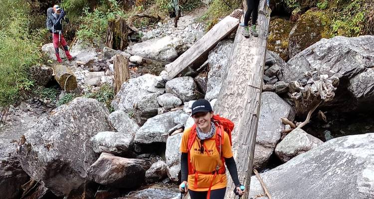 Hiker crossing a rocky stream using a log bridge.