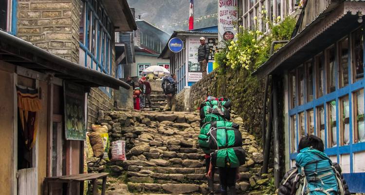 Turistas con mochilas subiendo escalones rocosos en un pueblo.