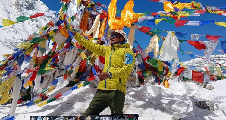 Individual posing with colorful prayer flags on snowy terrain.