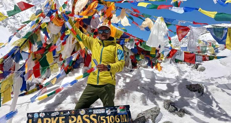 Individual posing with colorful prayer flags on snowy terrain.