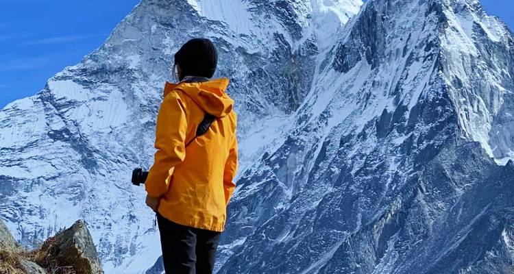 A person in a yellow jacket looking at snowy mountains, likely in Nepal.