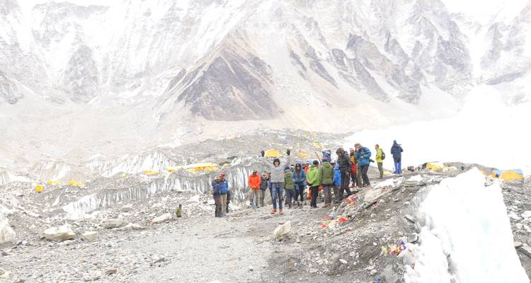 Group of people standing on a rocky terrain with tents in the background.