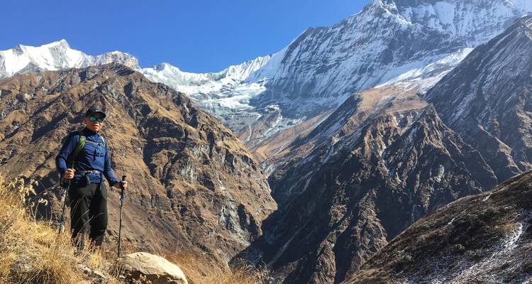 A person hiking in a mountainous region with snowy peaks in the background.