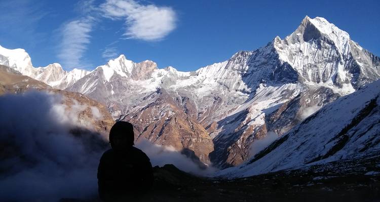 Person silhouetted against a majestic mountain backdrop at sunrise.