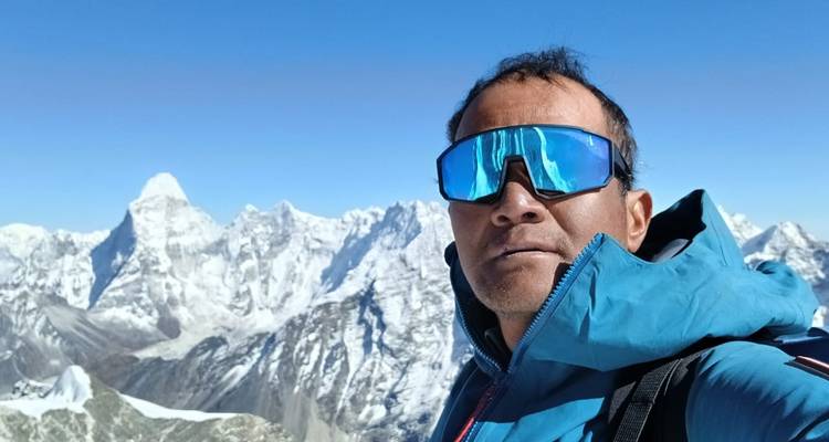 Person with sunglasses posing with snowy mountains in the background.