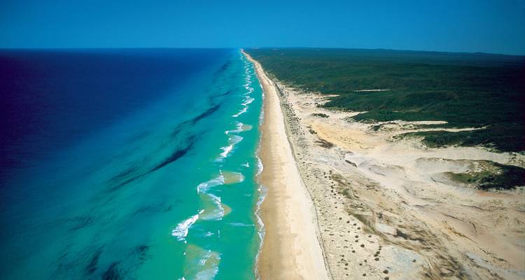 Vue aérienne d'une longue plage de sable bordée d'eaux océaniques bleu azur.