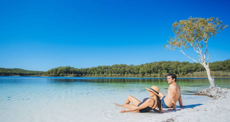 Una pareja relajándose en la playa junto a un lago con agua clara.