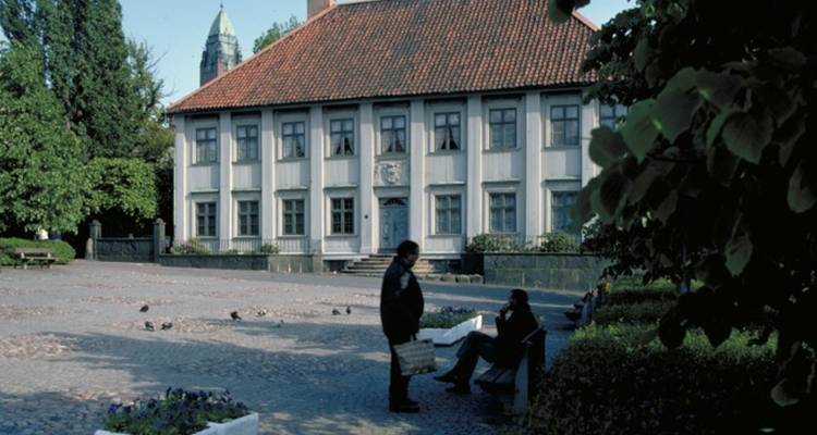 A street view with a historic building and people on benches.
