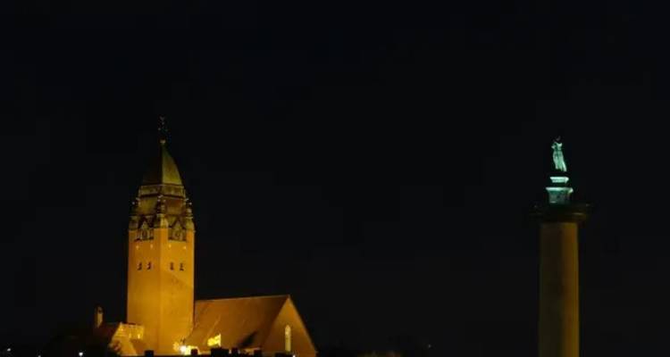 Night view of a church tower and a lighted column.