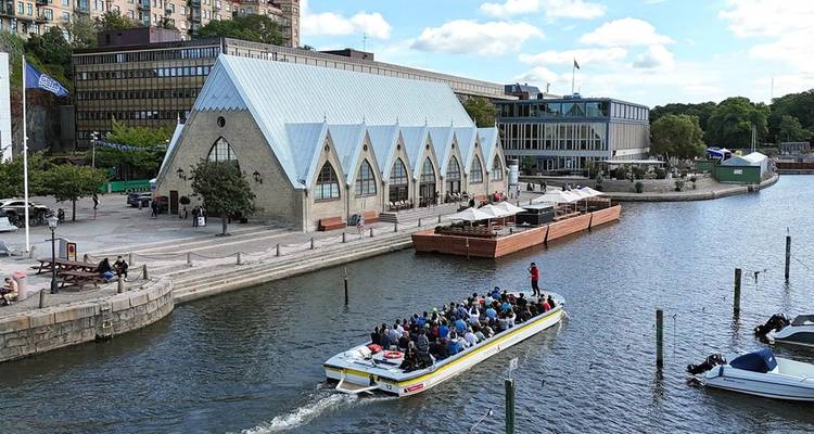 Tourists on a boat along a river, with a notable fish market building nearby.