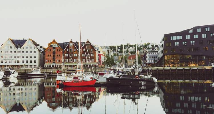 Vue du port avec des entrepôts en bois colorés et des bateaux se reflétant sur les eaux calmes de Tromsø.