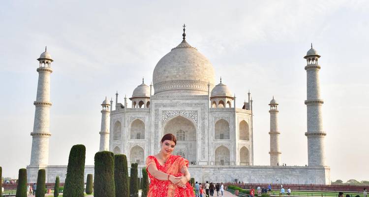 Besucherin im roten Sari, die freudig vor dem ikonischen Taj Mahal und den gepflegten Gärten posiert.