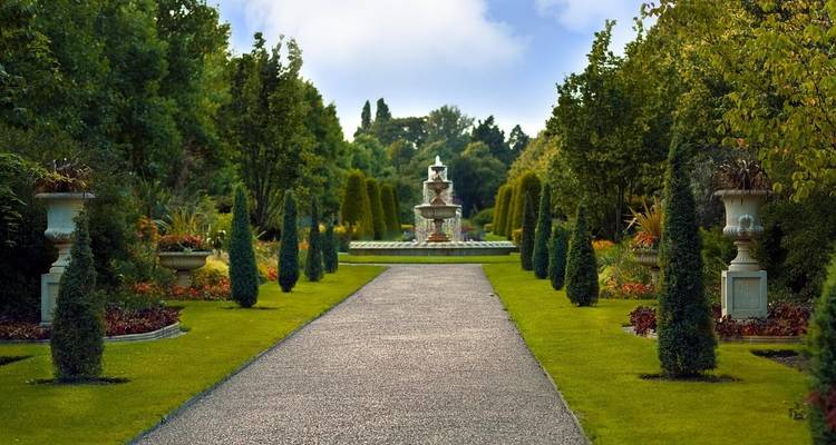 Gartenweg, der zu einem Springbrunnen mit gepflegten Hecken führt.