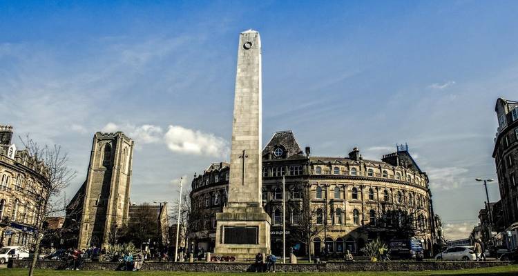 Belebter Stadtplatz mit einem Obelisken und historischen Gebäuden.