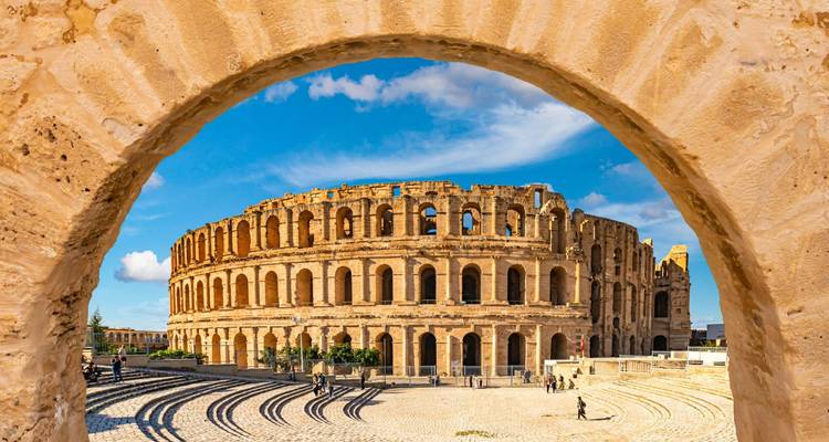 Ancient colosseum seen through an archway under a clear blue sky.