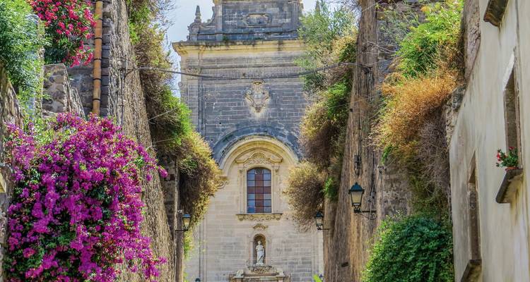 A narrow street with rich foliage and a historic building.