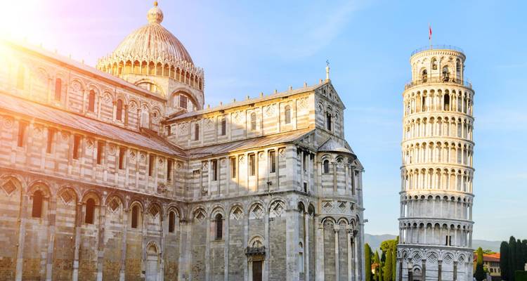 Sunlit façade of Pisa Cathedral beside the iconic Leaning Tower under blue sky.