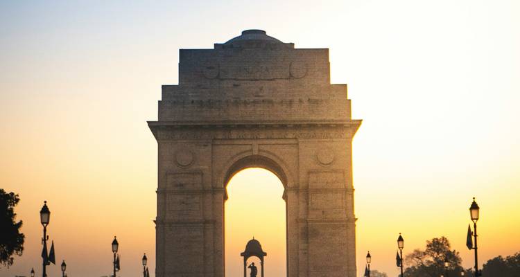 Silhouette of a large gate at sunset with lamp posts and trees.