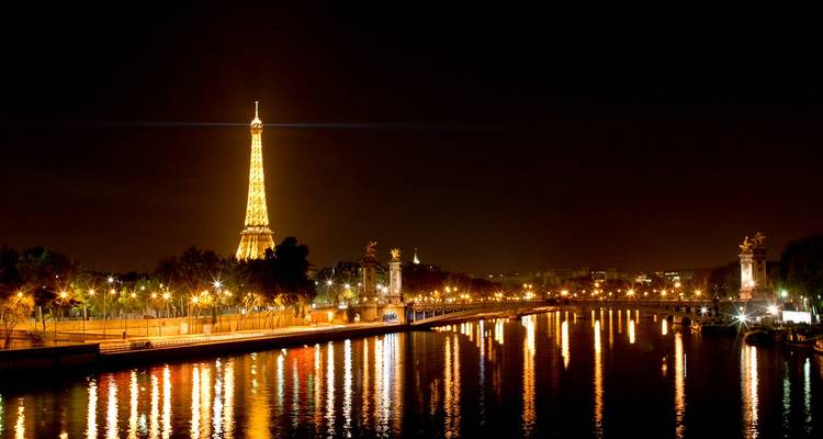 Eiffel Tower and the Seine River lit up at night.