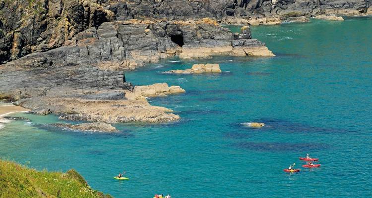Kayakers paddling in a turquoise bay with rocky cliffs.