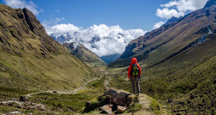 Randonneur en veste rouge regardant vers le bas d'une vallée entourée de montagnes
