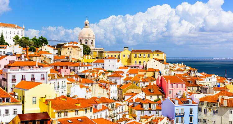 Colorful buildings with terracotta roofs overlooking water with distant hills.