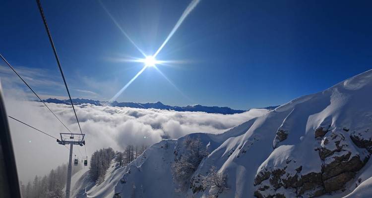 Scenic view of snowy mountain landscape with a ski lift and a bright sun.