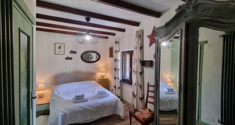 Cozy bedroom with a bed, lamps, and wooden furnishings under a beamed ceiling.