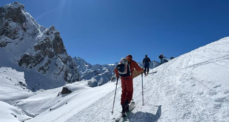 Group of skiers ascending a snowy slope with rocky mountains in the background.