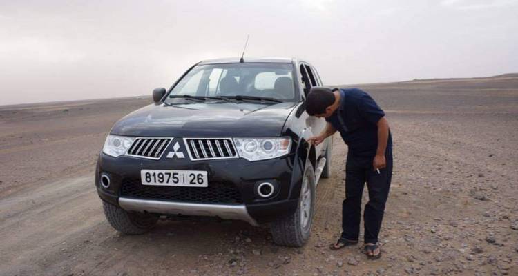 Homme inspectant une voiture dans un désert.