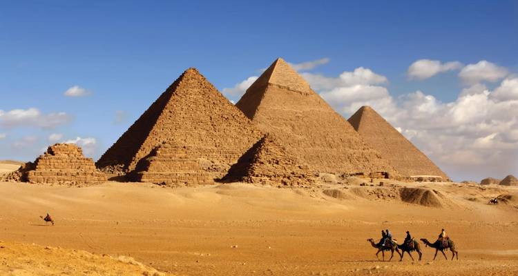 Die ikonischen Pyramiden von Giza erheben sich aus der Wüste, während Kamelreiter über goldene Sande wandern.